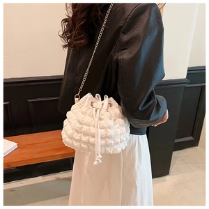 Détail du sac seau blanc plissé avec bandoulière en chaîne dorée porté par un modèle