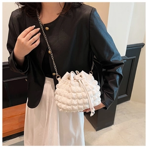 Détail du sac seau blanc plissé avec chaîne dorée porté par un mannequin élégant