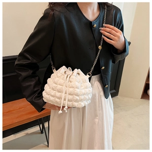 Détail d'un sac seau blanc avec texture matelassée, chaîne dorée et fermeture à cordon
