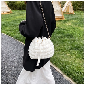 Détail du sac seau blanc à texture gaufrée avec bandoulière chaîne dorée sur un mannequin