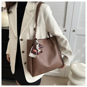 Detail einer braunen Ledertasche mit geflochtenem Griff und elegantem bedrucktem Seidentuch
