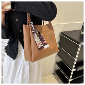 Detailansicht einer braunen Ledertasche mit geflochtenem Griff und gemustertem Seidenschal