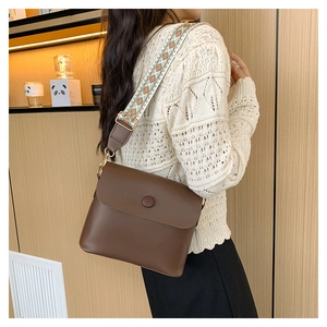 Close-up of brown leather crossbody bag with vintage geometric jacquard wide shoulder strap