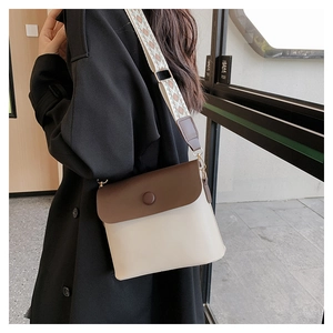 Detail of a contrast bucket bag with brown flap and geometric patterned wide strap