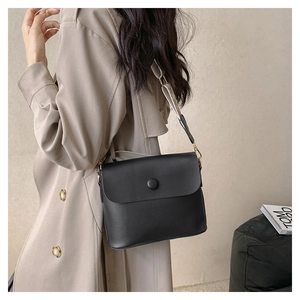 Detail of minimalist black leather crossbody bag with geometric wide strap on a trench coat