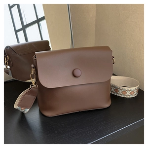 Close-up of brown crossbody bag with gold hardware and geometric patterned wide strap