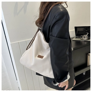 Detail of a large white canvas hobo bag with brown leather strap and brand logo patch