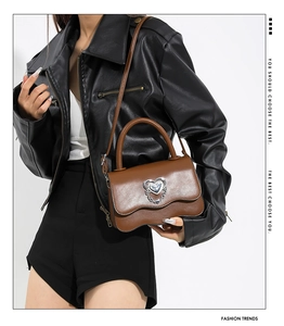 Detail of brown leather square bag featuring silver heart lock and wavy edge flap