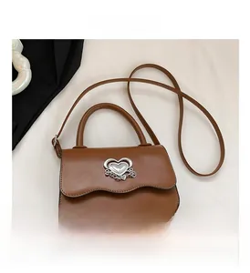 Detail of caramel crossbody bag featuring wave edge design and silver heart chain buckle