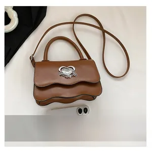 Detail view of wavy flap handbag with silver heart buckle and phone for size comparison