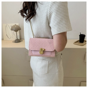 Détail du sac bandoulière rose avec texture écailles et fermoir doré porté par le mannequin