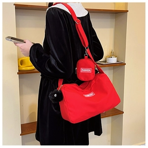 Detail of red crossbody bag with mini pouch and black pompom accessory on wide strap