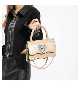 Detail of beige PU leather bag with silver heart metal buckle and wavy edge flap