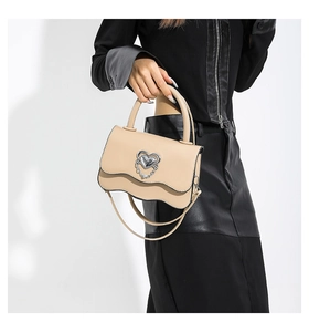 Detail of beige faux leather handbag with silver heart-shaped buckle and wave flap