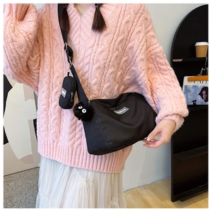 Detail of black nylon crossbody bag with small coin purse and plush charm on wide strap