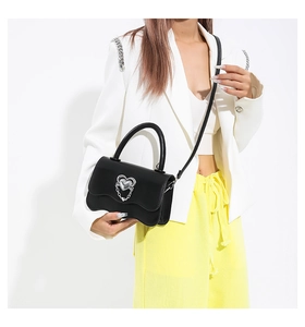 Fashionable black crossbody bag with silver heart charm on white blazer outfit