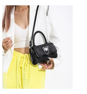 Detail of black wave-edge handbag with silver heart buckle and adjustable strap