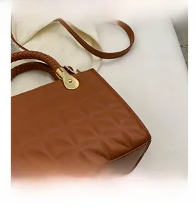 Close-up of brown quilted faux leather bag with woven handle and gold teardrop hardware