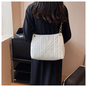 Detail of white quilted tote bag with gold chain strap worn on the shoulder