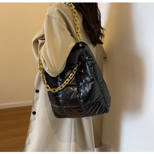 Detail of black quilted shoulder bag with gold chain strap on a beige trench coat