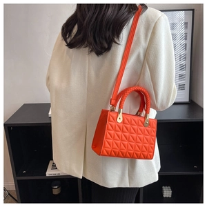 Detail of a bright orange quilted handbag featuring a woven handle and metallic chain accents