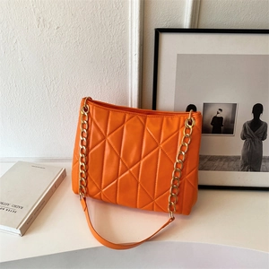 Detail of orange quilted tote bag with glossy finish and gold metal chain strap