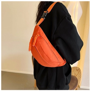 Detail of the vibrant orange crossbody bag showing woven zipper pulls and plastic buckle
