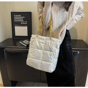 Detail of silver puffer tote bag with quilted pattern and gold chain strap on model