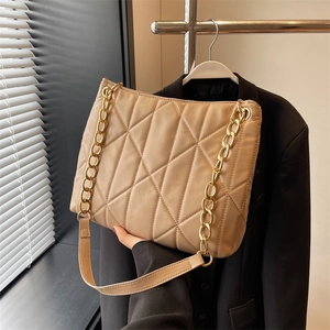 Detail of apricot quilted tote bag featuring a chunky gold metal chain strap and stitching