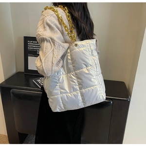 Detail of silver quilted tote bag with chunky gold chain strap shown on a model