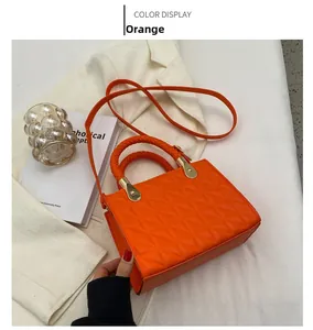 Detail of orange quilted handbag featuring woven handles and gold-tone hardware