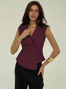 Detail of burgundy sleeveless V-neck top featuring waist pleats and asymmetric hemline