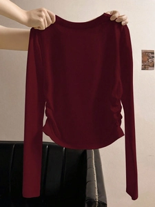 Dettaglio del design arricciato laterale su una t-shirt bordeaux aderente a maniche lunghe