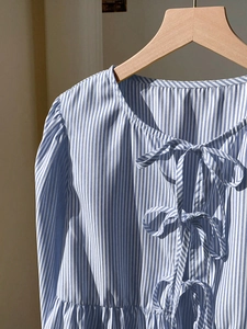 Détail d'une chemise à rayures bleues et blanches avec nœuds frontaux et manches bouffantes
