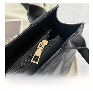 Detail of black quilted tote bag featuring golden metal zipper and textured leather finish