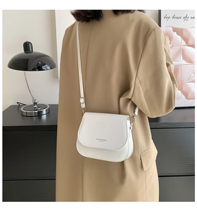 Modèle portant un petit sac besace blanc en cuir avec texte imprimé et bandoulière fine