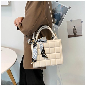 Detail of a beige quilted tote bag with a decorative silk scarf and adjustable strap