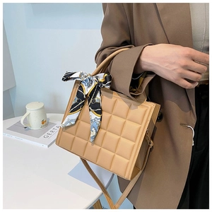 Detail of beige quilted tote bag with decorative blue silk scarf handle on a white table