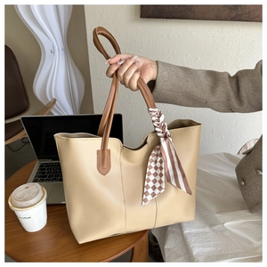 Detail of beige tote bag with dark brown handles and silk scarf in a modern office setting