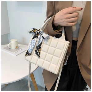 Detail of white quilted tote bag with silk scarf accessory and metal hardware