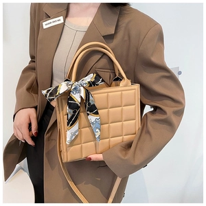 Detail of beige quilted tote bag featuring a decorative silk scarf and textured grid pattern