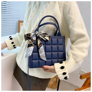 Detail of navy quilted tote bag with silk scarf on handle held by model in knit sweater