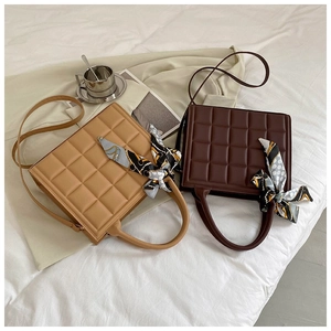 Detail of two quilted checkered tote bags with decorative silk scarves on white bedding