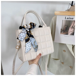 Detail of quilted beige tote bag with a patterned silk scarf on the top handle