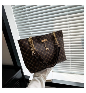 Close-up of retro monogram tote bag featuring gold chain and deer pendant detail