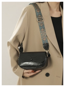 Detail of black glossy PU leather saddle bag with wide ethnic geometric patterned strap