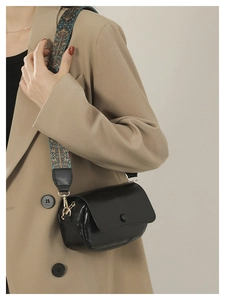 Detail of black PU leather saddle bag featuring a colorful bohemian woven shoulder strap