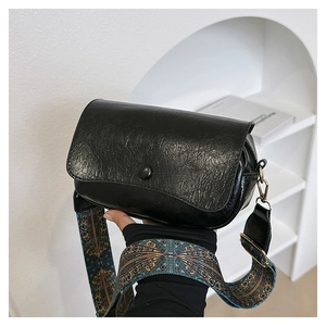 Detail of black textured PU leather saddle bag with ethnic geometric woven strap