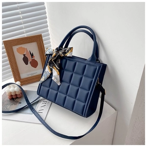 Detail of dark blue quilted tote bag with a silk scarf and adjustable strap on a minimalist background