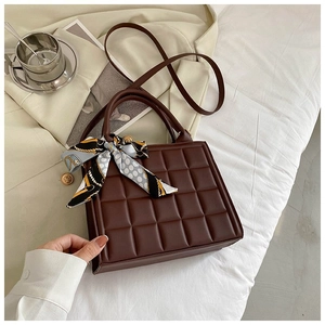 Close-up of brown quilted tote bag with silk scarf and leather texture on bed
